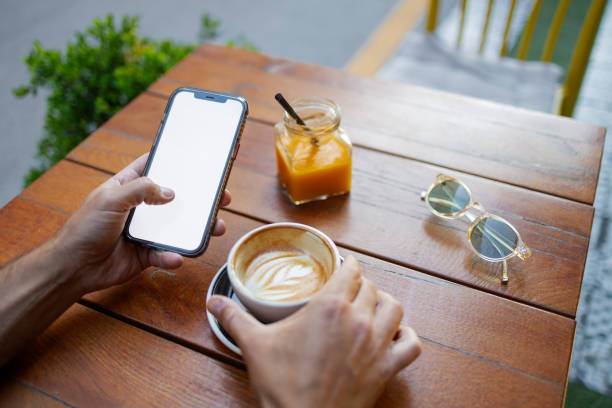 Man sits comfortably in a cozy coffee shop, holding his phone with the screen facing out, providing the perfect mockup space for your design or message. His relaxed posture and focused expression allow the blank phone display to take center stage, making this image ideal for showcasing app interfaces, advertisements, or promotional content in a casual, modern setting.