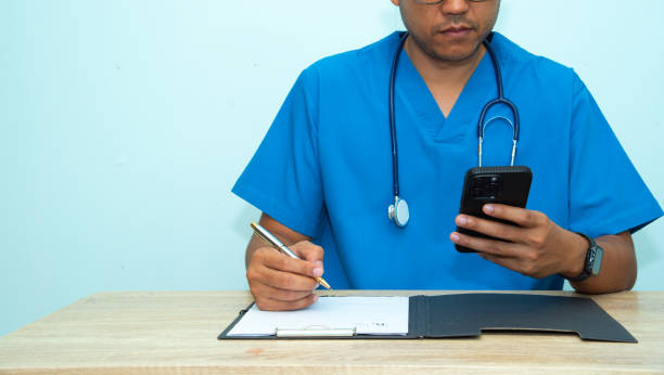 istock Smart medicine doctor working with computer notebook and medical text book at desk in the hospital.The physician, in the blue medical coat is filling out a medical record form.Medical concept 2187719255