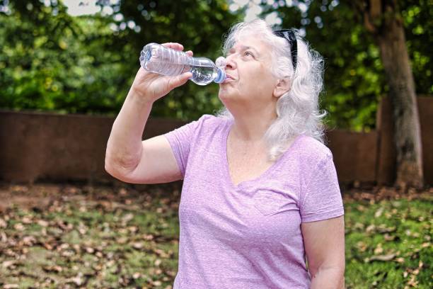 istock Gray-haired elderly lady drinks water from a bottle in the park. 2187721821