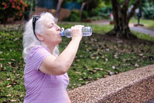 istock Gray-haired elderly lady drinks water from a bottle in the park. 2187721827