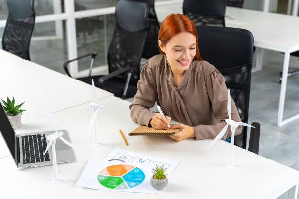 istock Young female engineer sitting at the table and looking at the wind turbine model 2187723075