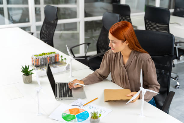 istock Young female engineer sitting at the table and looking at the wind turbine model 2187723094