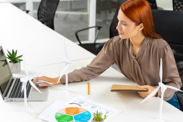 istock Young female engineer sitting at the table and looking at the wind turbine model 2187723111