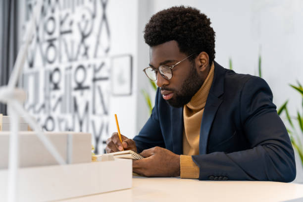 istock African american young architect sitting at the table and analyzing new model 2187723281