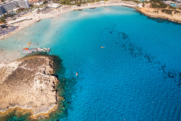 A stunning aerial view of a tropical coastline featuring clear turquoise waters, sandy beaches, anchored boats, and a scenic rocky island.