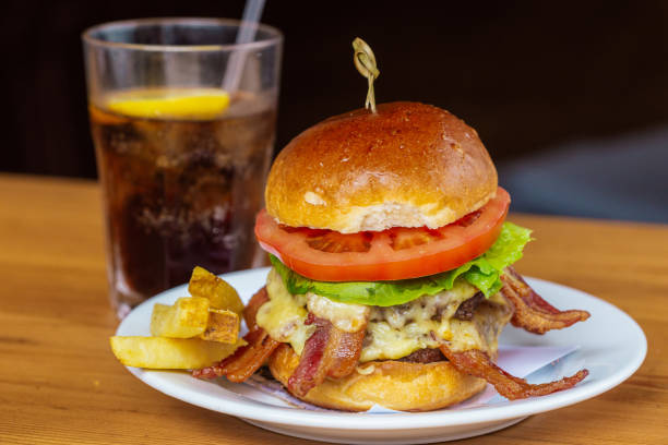 A mouth-watering bacon cheeseburger with fresh lettuce and tomato, served with crispy fries and a chilled glass of soda. Perfect for a sumptuous meal.