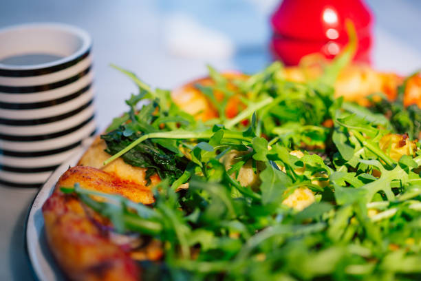 Close-up of a delicious pizza garnished with fresh arugula and roasted vegetables, accompanied by a cup and a red table setting. Ideal for showcasing healthy, vegetarian meal options.