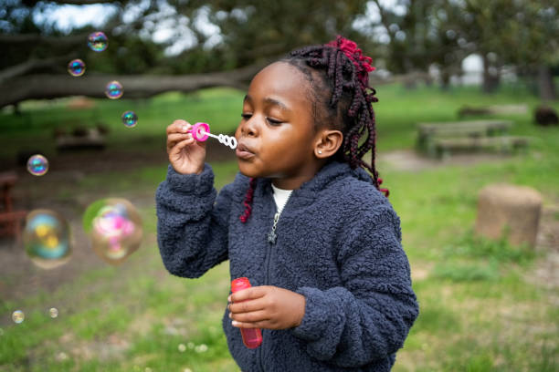 African small girl in warm clothing blowing bubbles at park on an autumn day