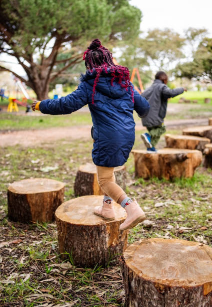 istock Children jumping across tree stumps outdoors at playground 2187741335