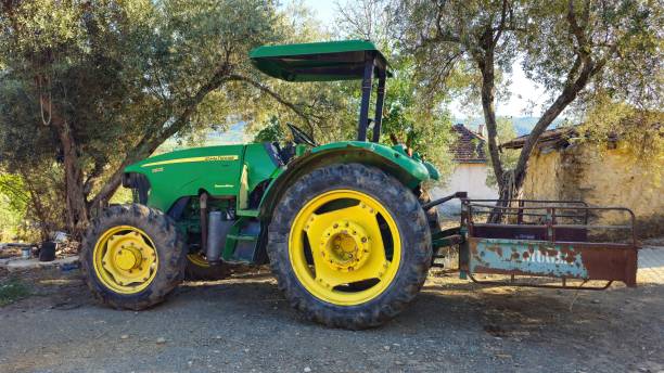 Mugla, Turkey - 17 Sep 2024: A green John Deere tractor with yellow tires sits in a field. John Deere is a company known for manufacturing agricultural, construction, and forestry machinery