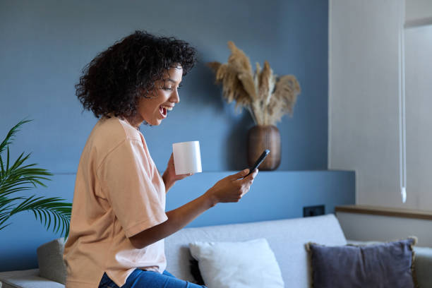 istock Excited latin woman using smartphone and drinking coffee at home 2187751093