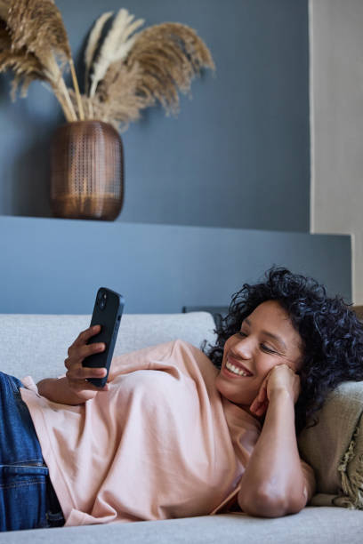 istock Latin woman relaxing on sofa using smartphone and smiling 2187751916