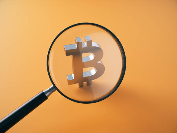 istock Magnifying glass in front of metallic Bitcoin symbol sitting on orange background. 2187753250