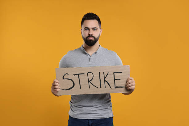 istock Man holding cardboard banner with word Strike on orange background 2187765053