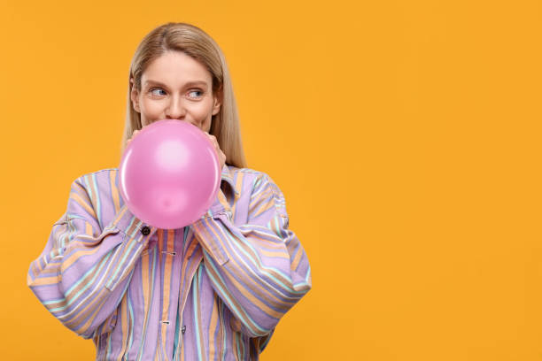 istock Woman blowing up balloon on yellow background. Space for text 2187765126