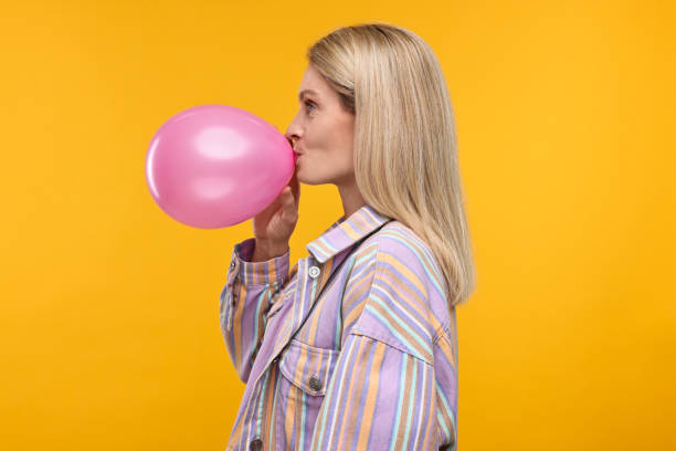 istock Woman blowing up balloon on yellow background 2187765150