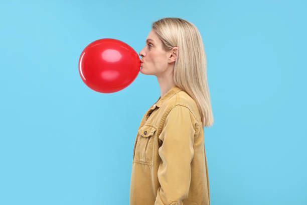istock Woman blowing up balloon on light blue background 2187765170