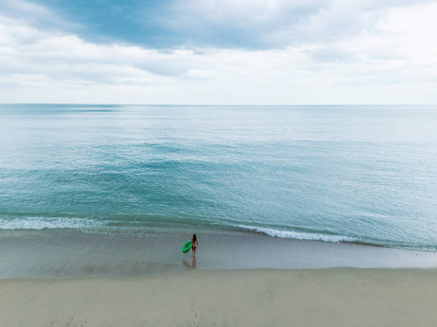 mulher em pé em uma praia arenosa segurando um anel inflável verde. - mulher feliz desfrutando de praia exótica no verão tropical de azul - fotografias e filmes do acervo