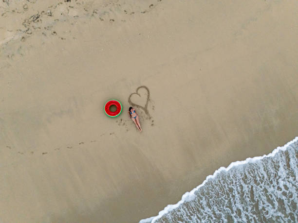 istock Woman Relaxing on Sandy Beach Beside Heart Drawing and Inflatable Ring 2187765920