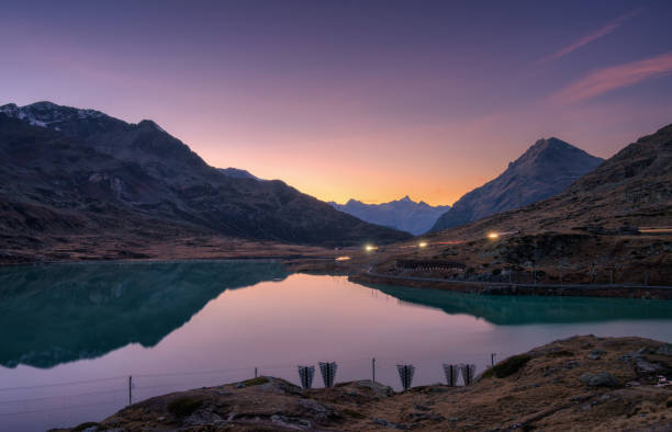 istock Sunset casts a serene glow on mountain peaks mirrored in a tranquil alpine lake in autumn. Lake Bianco, Switzerland in fall. Landscape with mountains, reflection in water, purple and orange sky. Dusk 2187772074
