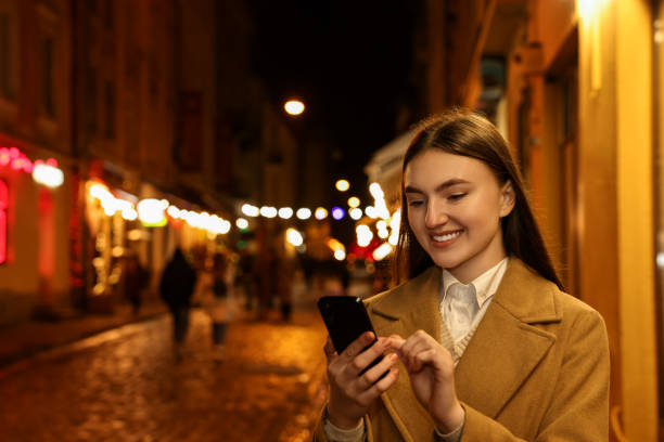 istock Smiling woman using smartphone on night city street. Space for text 2187774913
