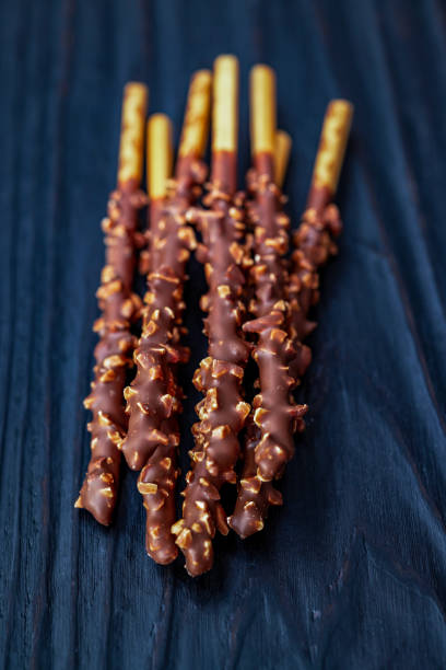 Close-up of chocolate Pocky sticks with a nut coating, arranged on a dark rustic wooden surface