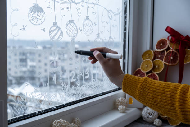 istock Creative enthusiastic unrecognizable woman in sweater paint window with white marker. Advent candle decoration on big clear window. Snowy winter outside 2187790145