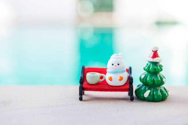 Miniature snowman with tea cup on red bench with Christmas tree over blurred background, Happy Christmas background idea