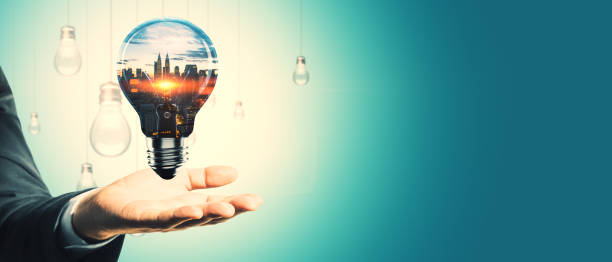 istock Hand holding a glowing lightbulb with cityscape inside and hanging bulbs in the background, symbolizing innovation and creative ideas. 2187792274