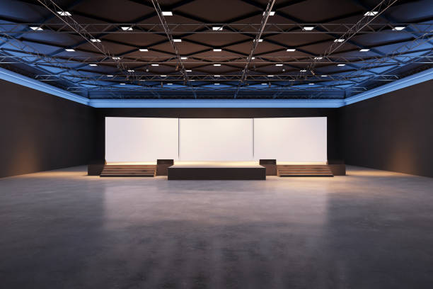 istock Modern exhibition space with a stage, white screens, steps, and a dark ceiling structure illuminated by lights. 3D Rendering 2187792645