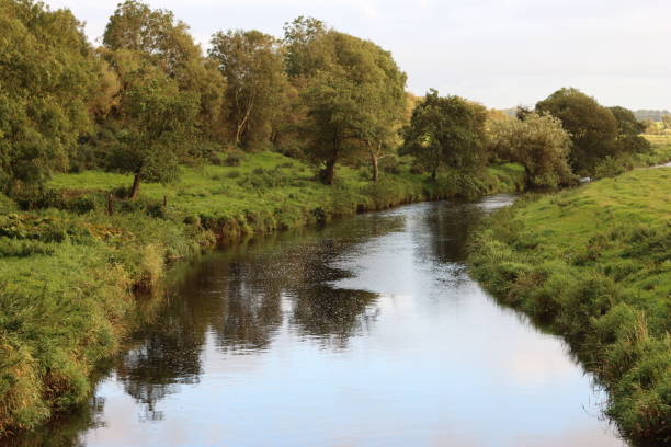 istock View along a river in summer, with trees lining the banks reflected in still water 2187792872