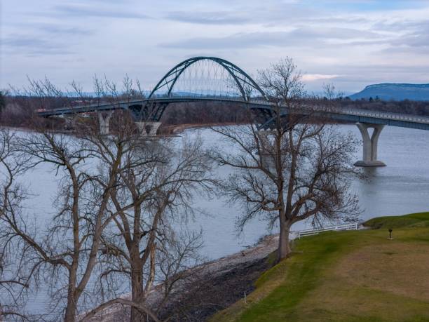 Bridge over river with bare trees and grassy banks.