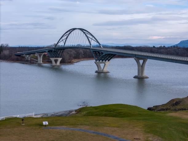 istock Modern arch bridge over calm river with cloudy sky. 2187795157