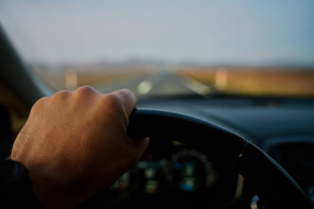 Male driver driving car, inside view. Man driving car on highway road at sunrise. Close-up of driver hands turning steering wheel