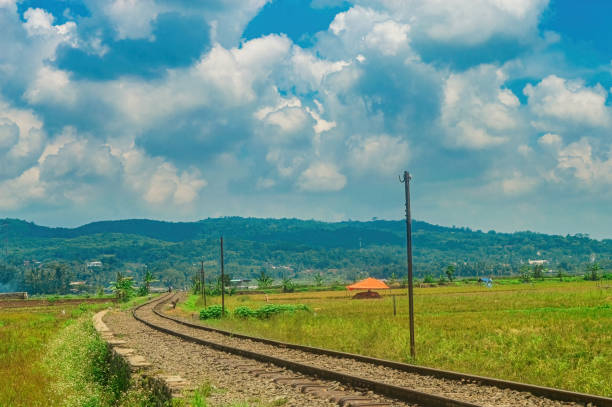 istock Scenic railway track curving through lush green fields with a backdrop of rolling hills and a vibrant blue sky filled with fluffy clouds. Perfect for travel and nature themes 2187797460
