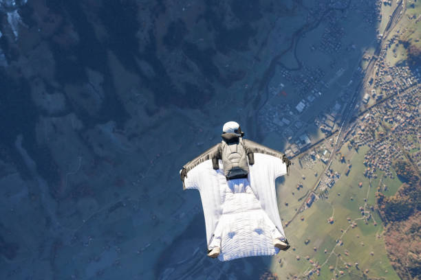 Wingsuit flier soars on his back above snowcapped mountains, Kandersteg Valley, Swiss Alps