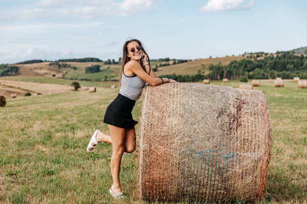 Portrait of carefree mid-adult redhead Caucasian woman leaning on a haystack, while enjoying the fresh and serene day in the nature