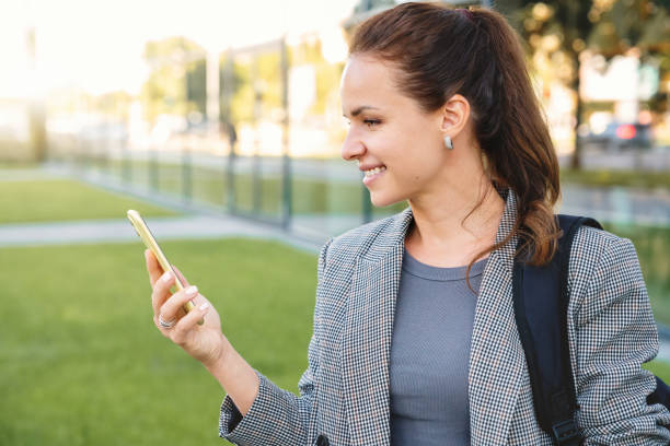 istock Caucasian businesswoman reading a message on her smartphone and smiling while standing on a city street. 2187804764