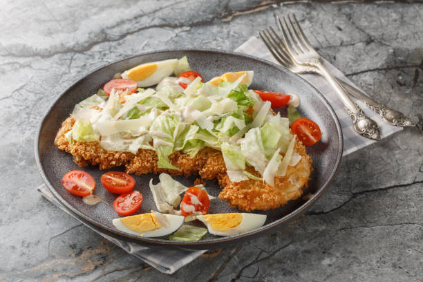 istock Breaded schnitzel Caesar salad with crispy chicken meat, eggs, parmesan, iceberg lettuce and tomatoes close-up in a plate. horizontal 2187818468