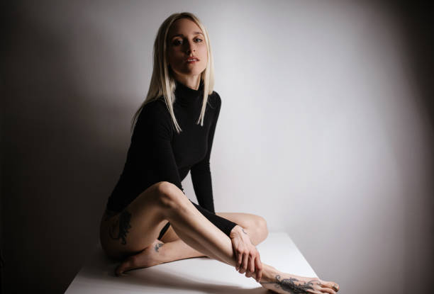 Close-up studio portrait of a 23 year old woman with long brown hair with a tattoo in a tank top on a gray background
