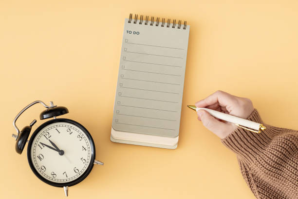 istock Creative layout made with woman's hand holding white pen, To do list in spiral notepad and retro alarm clock. Trendy pastel background, flat lay style. Planning concept. 2187823486