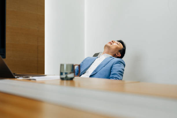 istock Overworked Asian businessman sitting at meeting room and sleeping, napping while working on laptop. 2187824771