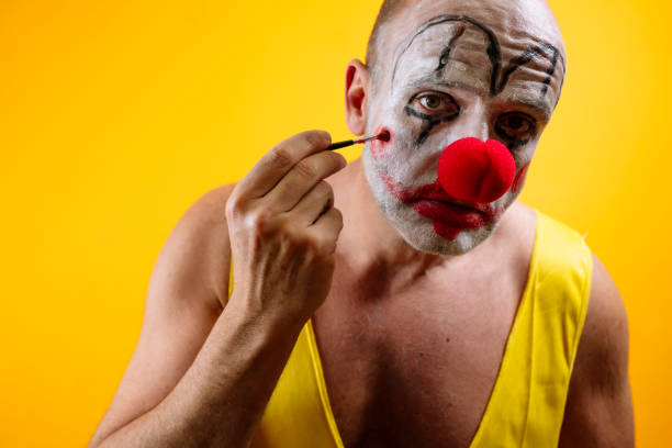 Sad clown applying makeup against yellow background.