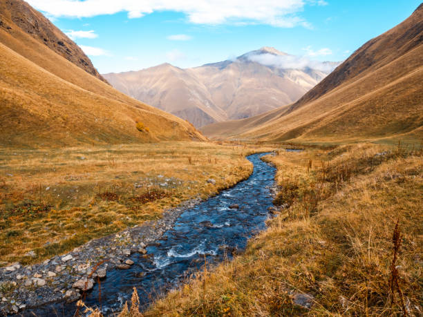 istock Fresh water stream as a leading lines between the yellow field and complex hills on autumn mountains background, walking view at Juta, Georgia. Dry grass on small mountain, beauty landscape. 2187827113