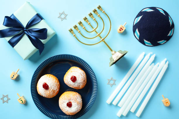 istock Vibrant Hanukkah celebration essentials on blue backdrop. Flat lay menorah, dreidels, sufganiyot, gift box, and kippah. Perfect for holiday-themed content 2187827786