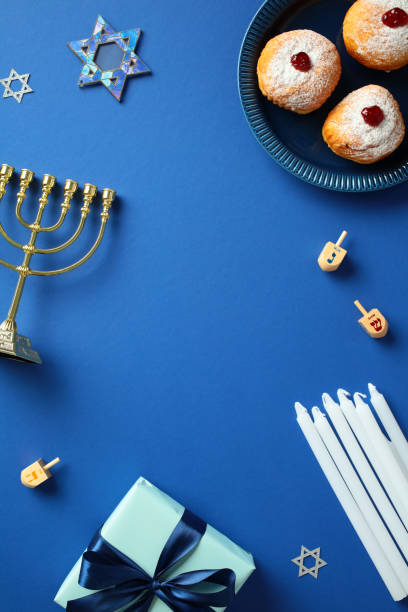 istock Hanukkah celebration essentials - menorah, dreidels, sufganiyot, gift box on blue background. Perfect for festive designs and Jewish holiday content. 2187827863