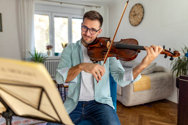 istock Man Playing Violin at Home with Music Sheet in Foreground 2187829609