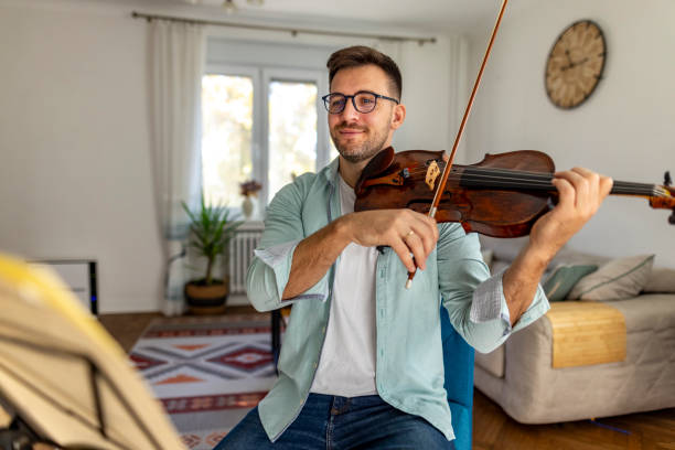 istock Young Man Playing Violin Indoors With Focused Expression and Sheet Music 2187829611