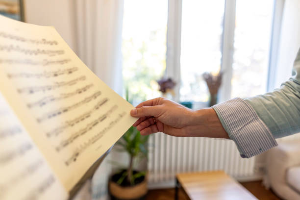 A close-up of a hand holding sheet music in a well-lit room with windows. The image captures a serene and focused atmosphere, perfect for concepts of practice, learning, or music study.