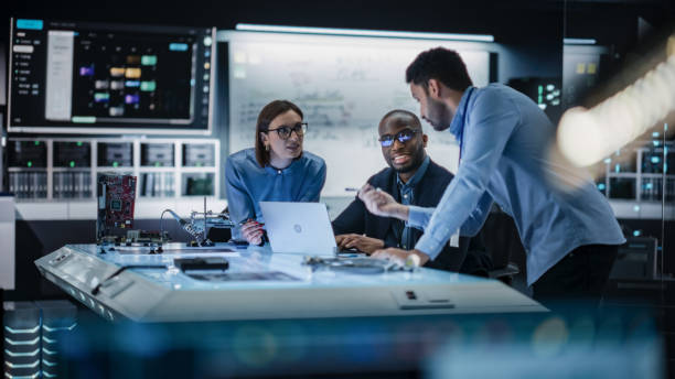istock Diverse Team of Engineers Collaborating on Manufacturing Project in a Research Facility. Colleagues Analysing Data Using Laptop Computer and Brainstorming for a Technologically Advanced Invention 2187841564